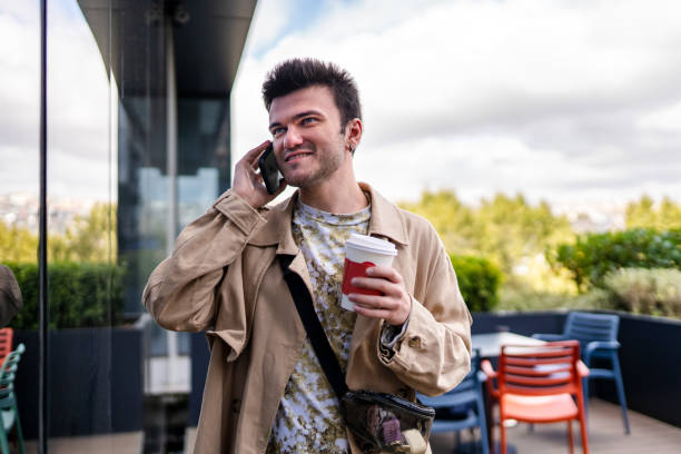 young man holding coffee in cardboard cup and talking on phone